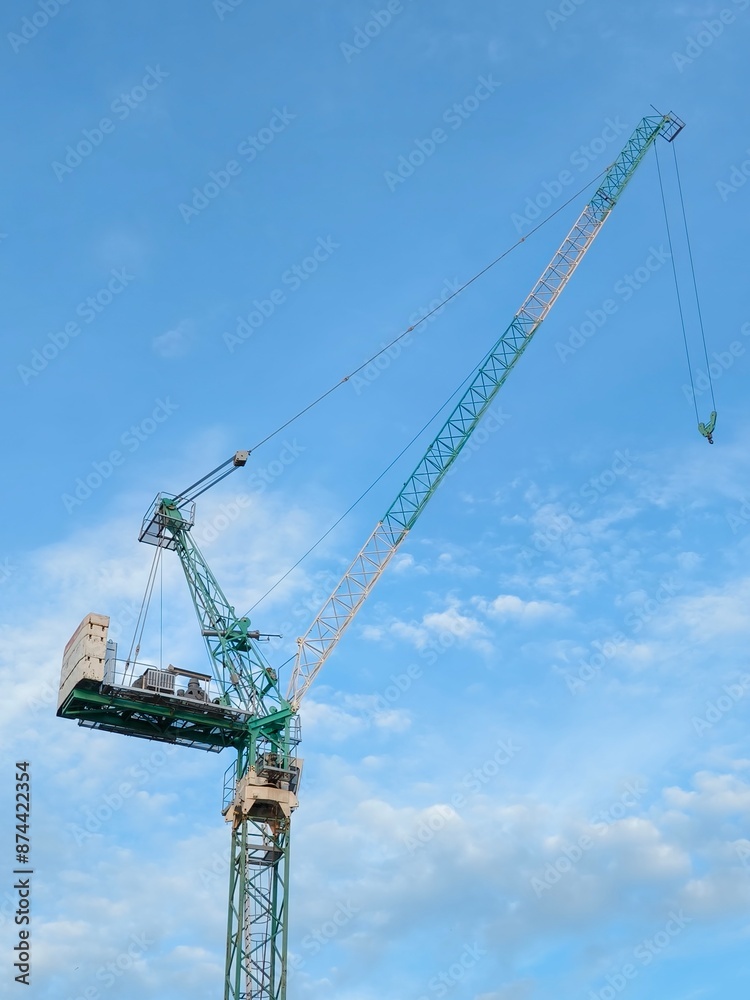 It is yellow tower crane working in sunny day. There are clouds in blue sky. It is close up view. It is midday time. Shot from below of crane that puts down on ground wheelbarrow full of industrial. It is yellow tower crane working in sunny day. There are clouds in blue sky. It is close up view. It is midday time. Shot from below of crane that puts down on ground wheelbarrow full of industrial.