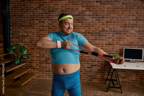Canvas Print Comic chubby man in sportswear fooling around with fitness equipment