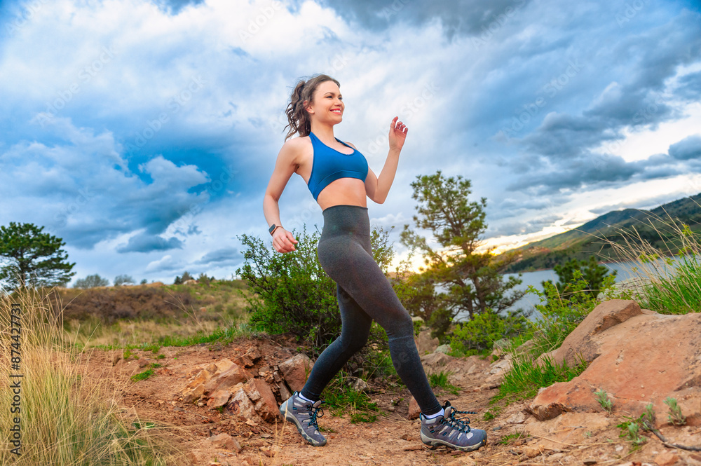 Young woman running on rocky trail with mountains in background Young woman running on rocky trail with mountains in background