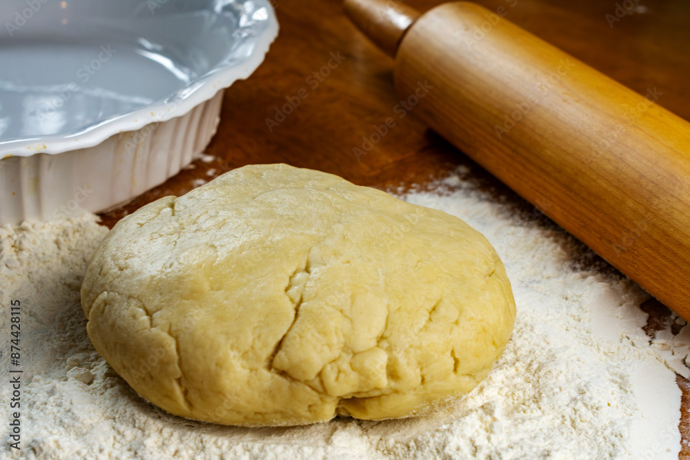 Making a pie. Getting ready to make a pie. Dough on a floured wooden surface. Pie plate and wooden rolling pin in background. Making a pie. Getting ready to make a pie. Dough on a floured wooden surface. Pie plate and wooden rolling pin in background.