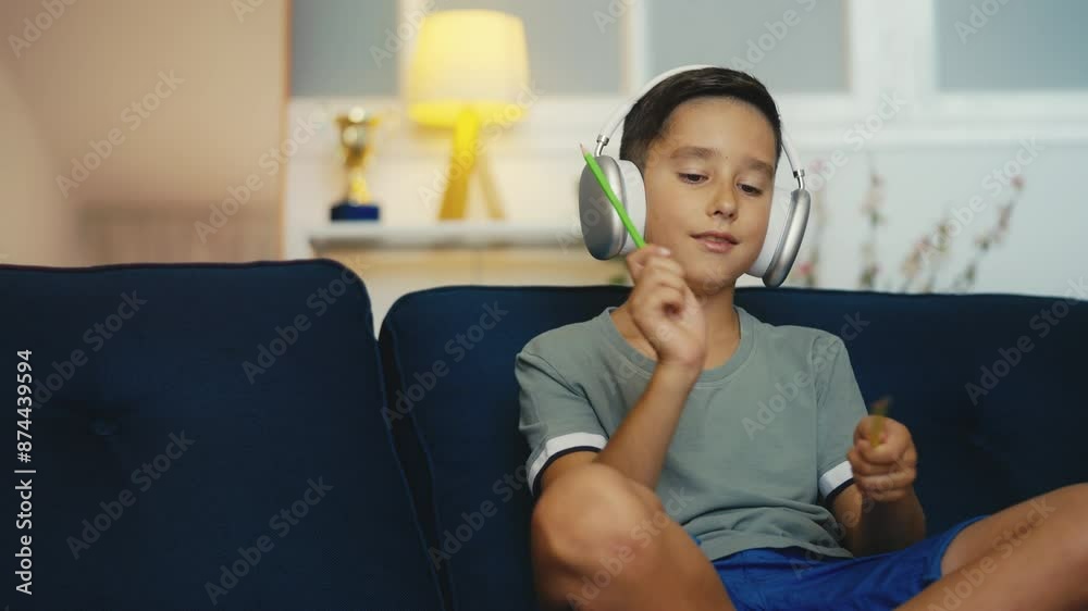 Young boy wearing headphones plays imaginary drums with pencils, musical hobby Young boy wearing headphones plays imaginary drums with pencils, musical hobby