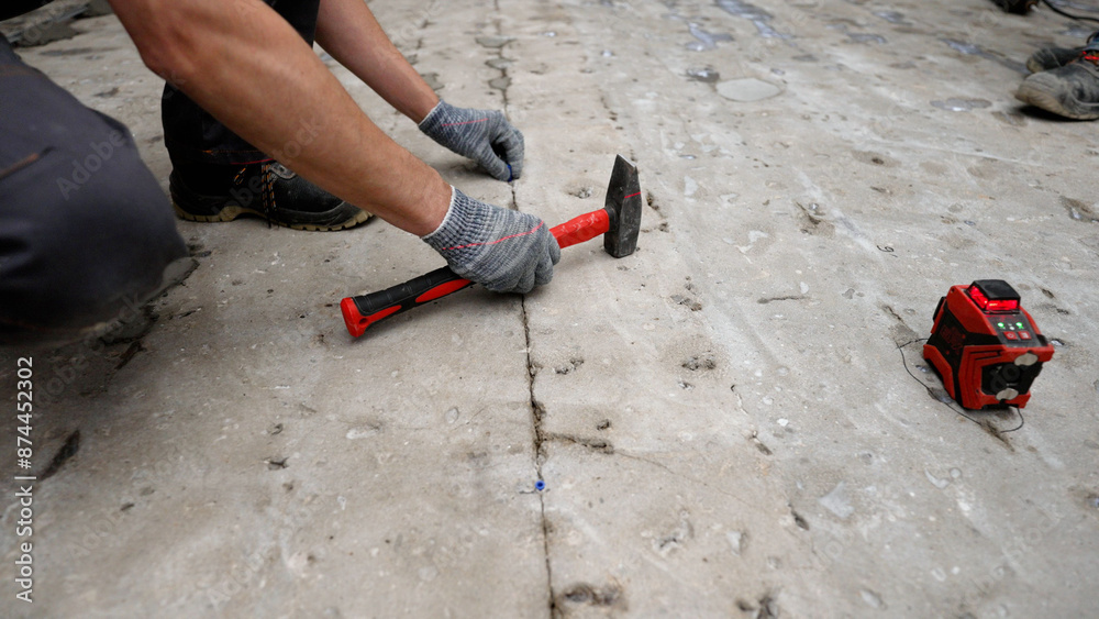 The master uses a hammer to hammer a dowel into the concrete floor. Repairing the floor, hammer in the dowel before pouring the floor. Concrete floor, installation of metal controls. The master uses a hammer to hammer a dowel into the concrete floor. Repairing the floor, hammer in the dowel before pouring the floor. Concrete floor, installation of metal controls.