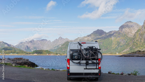 A motorhome with bicycle parked by fjord in Lofoten, Perfect for an adventure road trip. Stunning mountain views and clear skies create a beautiful scene. Lofoten Islands, Norway