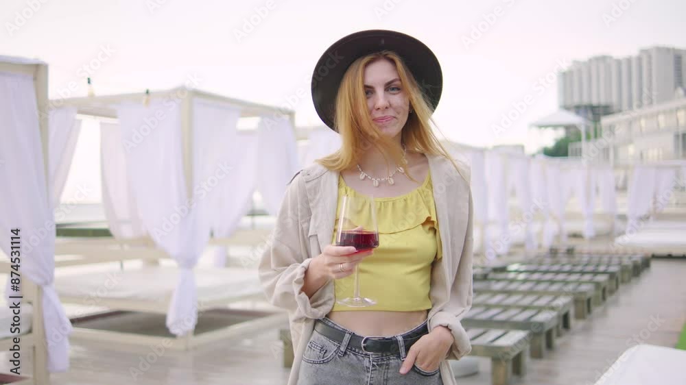 A woman wearing a hat and yellow top is enjoying a drink at summer resort on rainy sunrise A woman wearing a hat and yellow top is enjoying a drink at summer resort on rainy sunrise