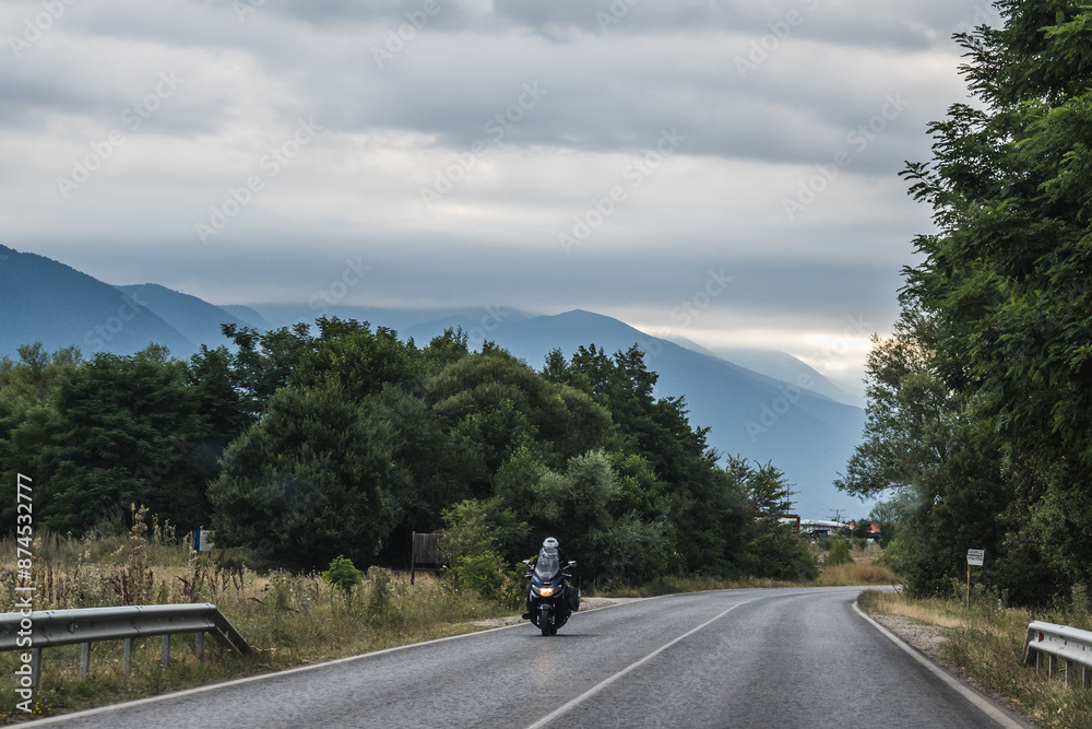 A lone biker drives his motorcycle along a highway that runs through the beautiful mountainous landscape of Bulgaria A lone biker drives his motorcycle along a highway that runs through the beautiful mountainous landscape of Bulgaria