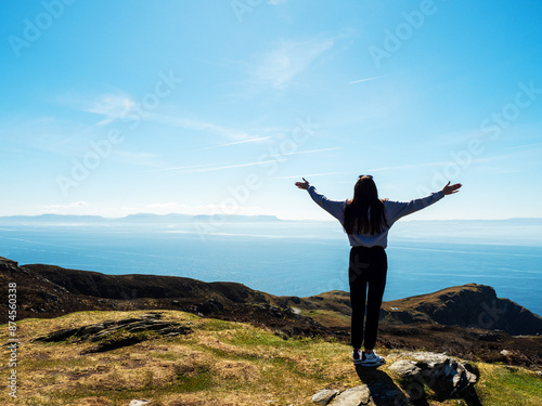 Young teenager girl exploring beautiful Sliabh Liag, county Donegal, Ireland, Benbulben in the background. Travel and tourism. Warm sunny day. Stunning Irish nature landscape scene in the background. photo