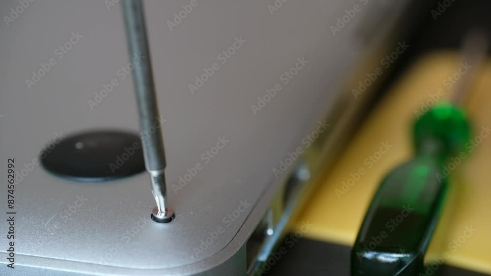 Technician carefully unscrews bolts from laptop closeup. Each screwdriver turn bringing device closer to being dismantled for repair