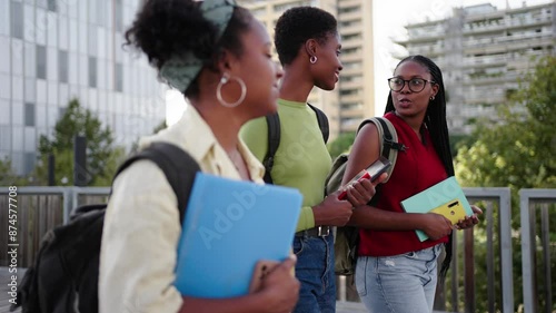 Side view of group of only black female college students on way to university campus. Three young African American happy women friends walk relaxed chatting with backpacks and books through city
