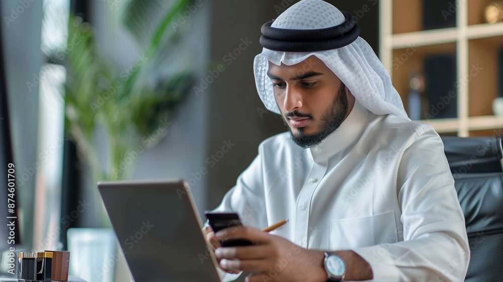 Young muslim man businessman sitting in office at desk and using mobile phone and credit card Young muslim man businessman sitting in office at desk and using mobile phone and credit card