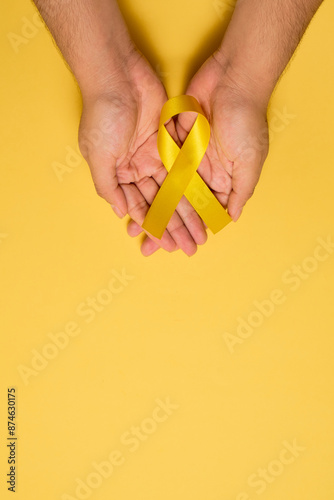 Female hands hold yellow ribbon for Suicide Prevention Day or Childhood Cancer Day, with copyspace