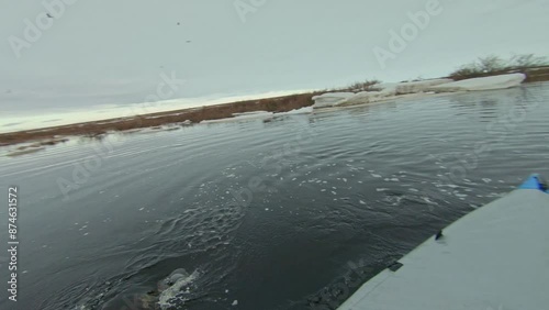A kayaker paddles through a river with melting ice, navigating through floating chunks of ice in the spring