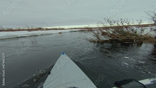 A kayak floats down a river, surrounded by snow melting on the banks