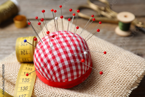 Checkered pincushion with pins and other sewing tools on wooden table, closeup