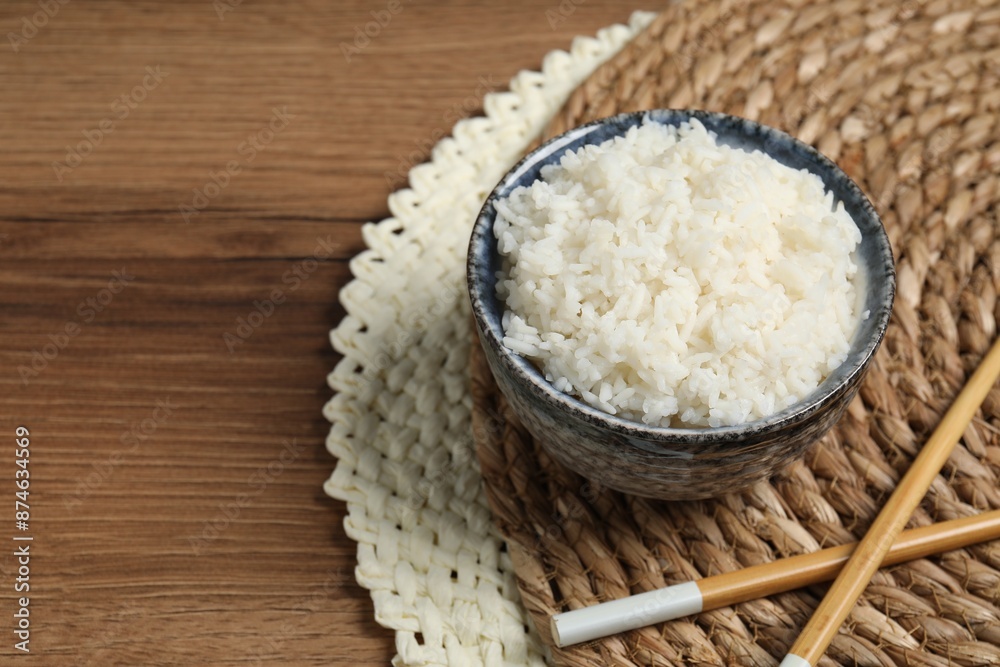 Tasty cooked rice in bowl and chopsticks on wooden table, space for text