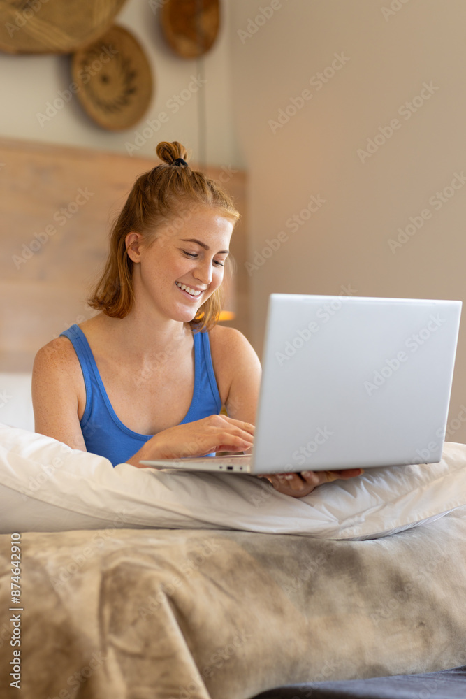 Smiling woman using laptop while sitting on bed, working from home Smiling woman using laptop while sitting on bed, working from home