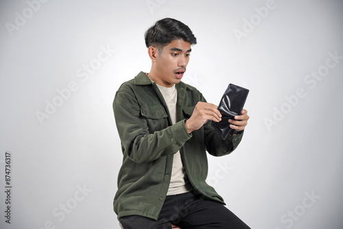 No money. Depressed young Asian man in casual shirt looking at empty wallet, having financial problems isolated on white background