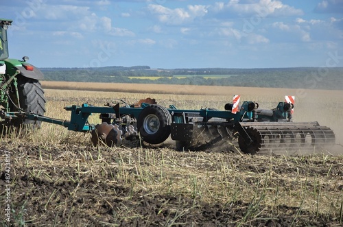 the tractor processes the field with a disc harrow after harvesting. agricultural work in the field on a summer day