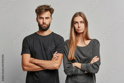 Serious man and woman standing with crossed arms in gray attire, portraying determination and confidence with a neutral background.