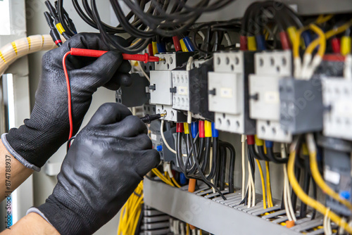 Electrician holding electrical measuring tool meter on panel circuit breaker power electricity switchboard system cabinet for repairing or safety service maintenance and electric cable wiring check.