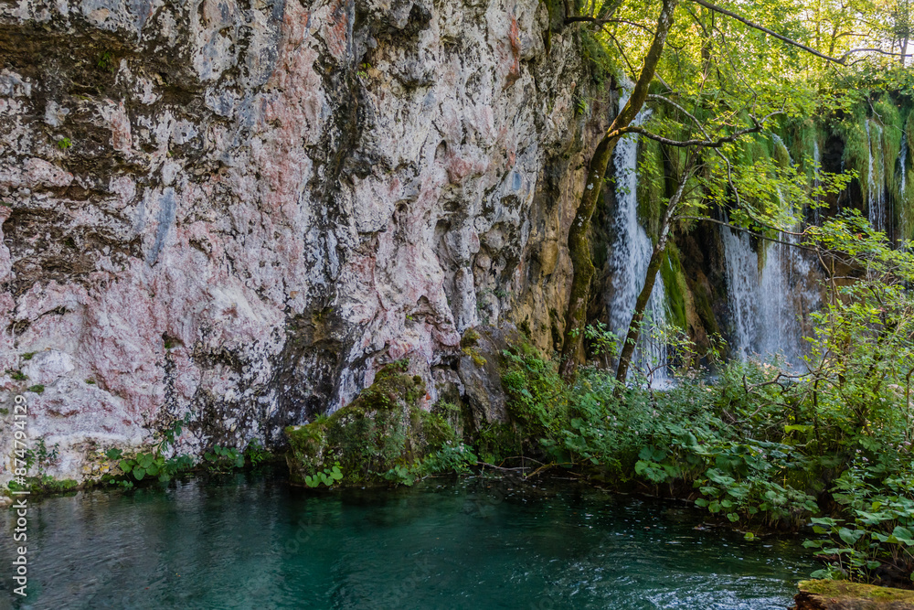 Clear waters with a small waterfall flowing down rocky cliffs amidst green foliage, highlighted by sunlight, in Croatia Clear waters with a small waterfall flowing down rocky cliffs amidst green foliage, highlighted by sunlight, in Croatia
