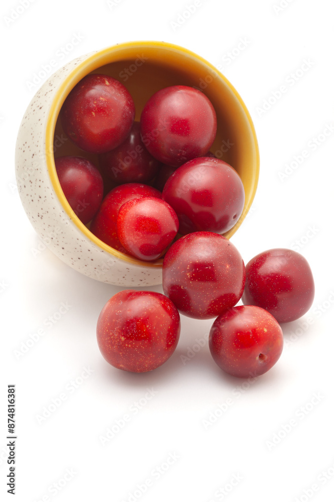 Front view of fresh Cherry Plum (Prunus cerasifera) fruits spilled out from a ceramic bowl on a white background. Front view of fresh Cherry Plum (Prunus cerasifera) fruits spilled out from a ceramic bowl on a white background.