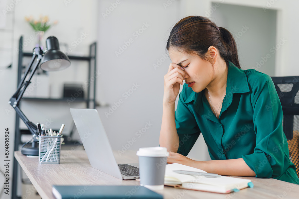 Stressed woman working at home desk, looking at notebook and laptop, managing tasks in home office.