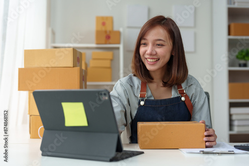 SME entrepreneurs, small businesses Online sales concept, happy Asian female business owner working on laptop computer and parcel boxes. Delivery of SME parcel boxes to customers Confirm order.