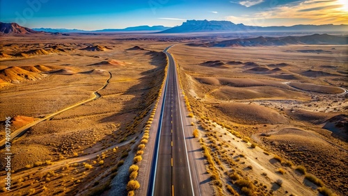 Aerial view of a vast, winding empty asphalt road stretching into the horizon of a scenic desert landscape.