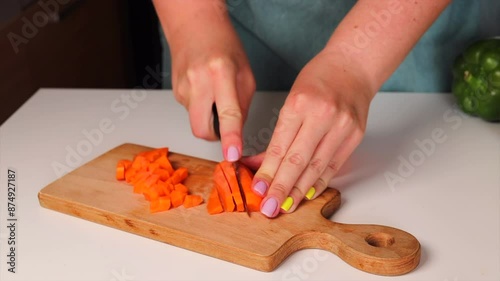 A woman in a beautiful apron is dicing carrots with a knife on a wooden chopping board. Cooking in the kitchen. The process of making cabbage rolls.