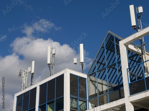 Mobile radio antennas on the roof of a modern office building with gables and spacious windows. Relentless to maintaining the communications network.