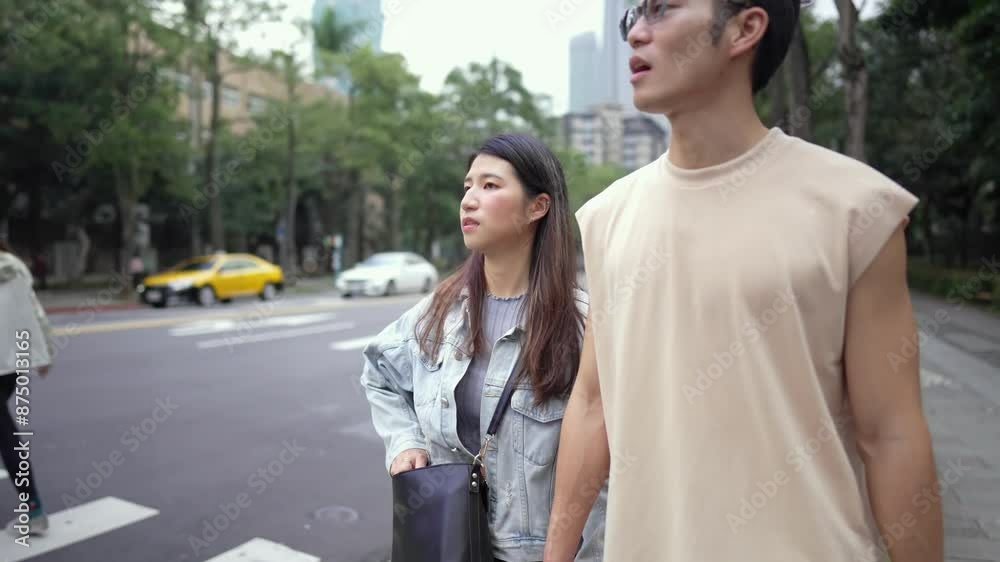 A young Taiwanese couple in their twenties walking through the streets of Xinyi District, Taipei City at noon in spring. The man is wearing a sleeveless top, and the woman is wearing a denim jacket. A young Taiwanese couple in their twenties walking through the streets of Xinyi District, Taipei City at noon in spring. The man is wearing a sleeveless top, and the woman is wearing a denim jacket.