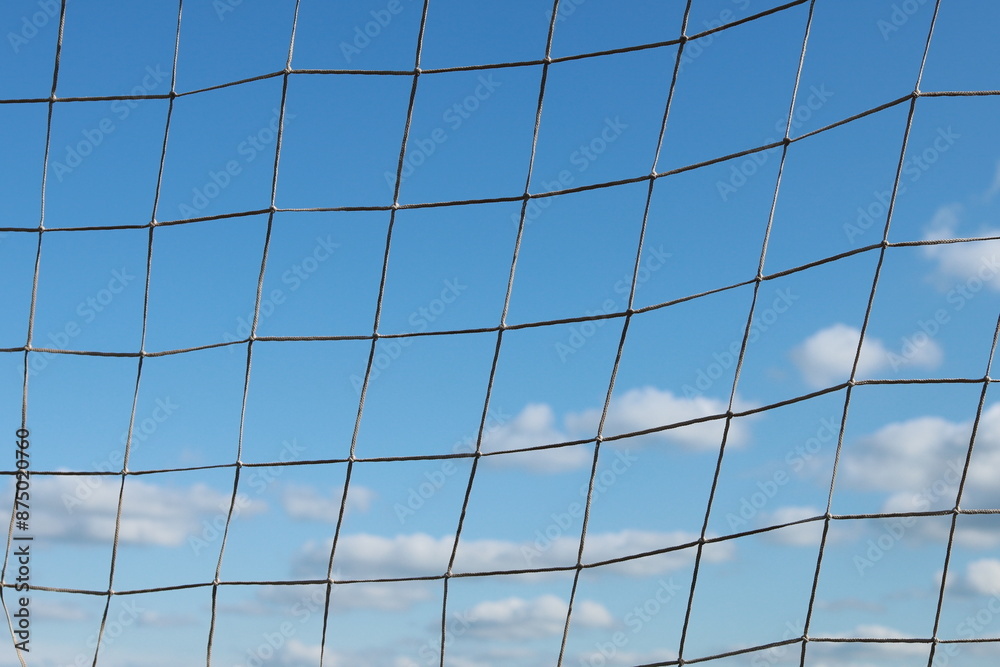 A close-up of a football goal net with a sky with fluffy clouds in the background A close-up of a football goal net with a sky with fluffy clouds in the background