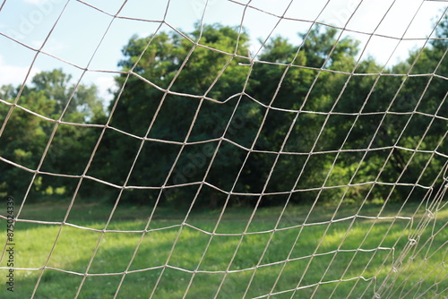 A close-up of a football goal net on a grass pitch with trees in the background. Capturing the essence of local sports. photo