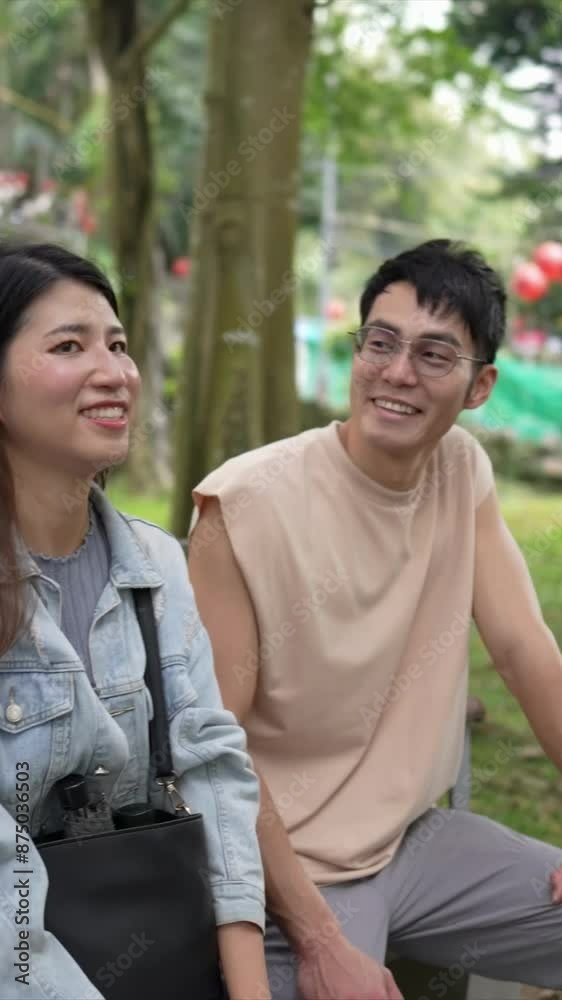 A vertical video of a young Taiwanese couple in their twenties sitting on a bench and talking in a park in Xinyi District, Taipei City, on a spring afternoon. The man is wearing a sleeveless top A vertical video of a young Taiwanese couple in their twenties sitting on a bench and talking in a park in Xinyi District, Taipei City, on a spring afternoon. The man is wearing a sleeveless top