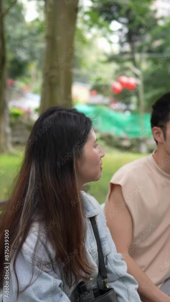 A vertical video of a young Taiwanese couple in their twenties sitting on a bench and talking in a park in Xinyi District, Taipei City, on a spring afternoon. The man is wearing a sleeveless top A vertical video of a young Taiwanese couple in their twenties sitting on a bench and talking in a park in Xinyi District, Taipei City, on a spring afternoon. The man is wearing a sleeveless top