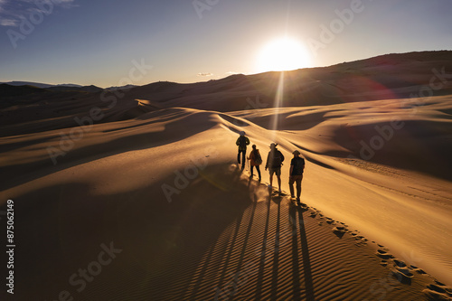 Group of hikers are walking at sunset desert dune. Long beautiful shadows on sand dunes