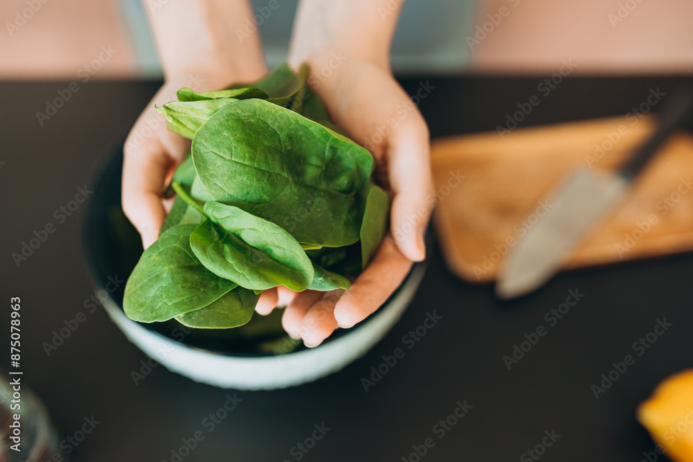 A green spinach in woman hands in kitchen at home. Raw food diet and healthy eating concept. Top view. Menu, recipe book banner