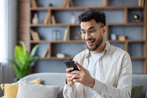 Sticker Close-up photo of a happy young Indian man at home using a mobile phone, looking