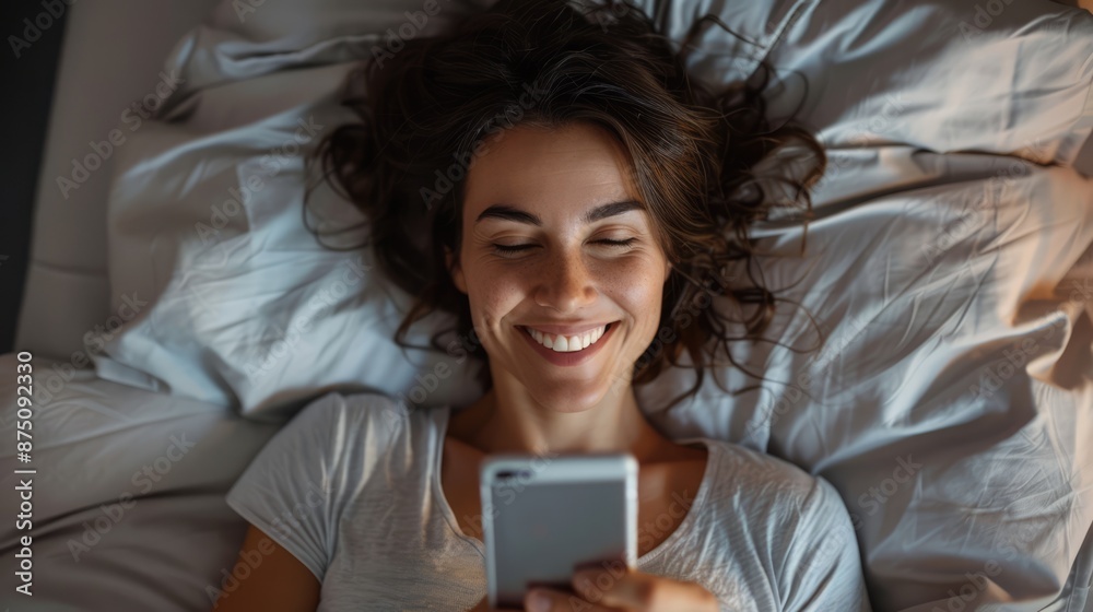 a mature smiling caucasian woman lying in bed, looking at her cell phone a mature smiling caucasian woman lying in bed, looking at her cell phone
