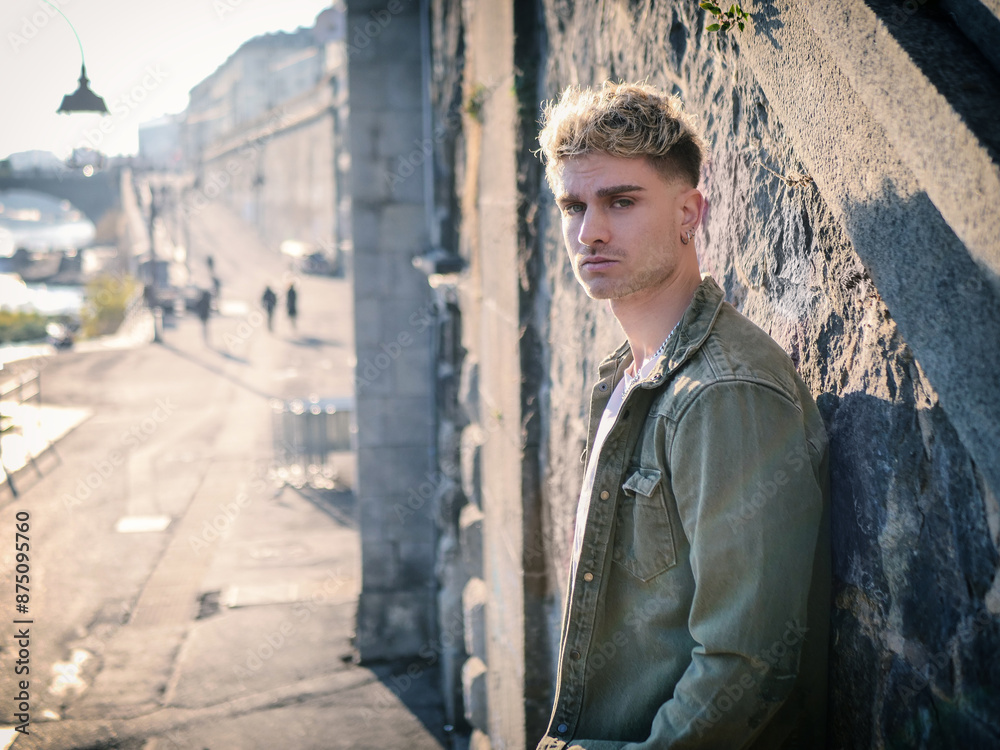 A young man wearing casual clothing leans against a weathered stone wall. He appears relaxed, with his arms crossed and a thoughtful expression on his face. The texture of the wall contrasts with his A young man wearing casual clothing leans against a weathered stone wall. He appears relaxed, with his arms crossed and a thoughtful expression on his face. The texture of the wall contrasts with his