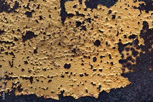 A close-up shot of a surface covered in peeling gold paint, revealing the rust beneath. The texture is rough and uneven, with patches of paint clinging to the metal.