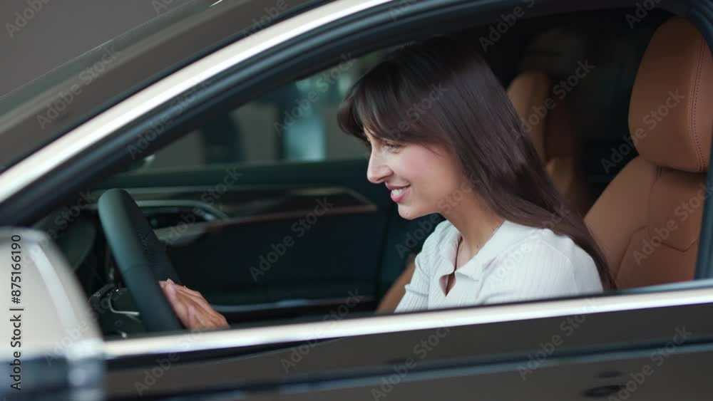 Side view of Caucasian client comfortably sitting inside luxury car. Satisfied woman happy while observing automobile in auto salon. Gently stocking steering wheel with both hands. Rich buyer. Side view of Caucasian client comfortably sitting inside luxury car. Satisfied woman happy while observing automobile in auto salon. Gently stocking steering wheel with both hands. Rich buyer.