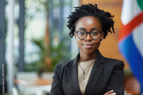 A confident young businesswoman wearing glasses stands indoors, exuding intelligence and elegance, with an assured expression and a professional demeanor, ready for success.