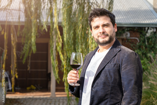 Hombre apuesto tomando una copa de vino mientas sonrie con confianza a cámara photo