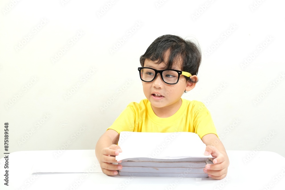 A young boy in a yellow shirt and black glasses, sitting at a table with a stack of books, looking engaged. Perfect for educational materials, promoting literacy,school projects, and tutoring services A young boy in a yellow shirt and black glasses, sitting at a table with a stack of books, looking engaged. Perfect for educational materials, promoting literacy,school projects, and tutoring services