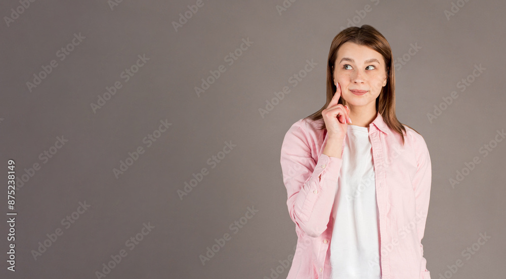 Thoughtful woman keeps hand on cheek looks pensively above dressed in casual clothes poses against gray background blank copy space for your advertising content thinks about future Thoughtful woman keeps hand on cheek looks pensively above dressed in casual clothes poses against gray background blank copy space for your advertising content thinks about future