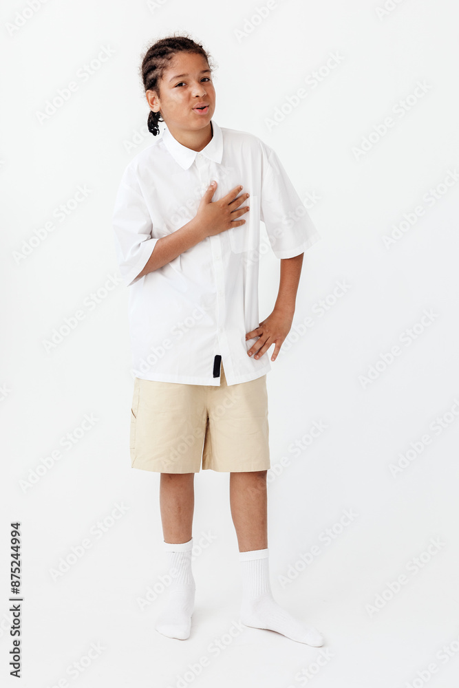 Fototapeta premium Young boy in trendy outfit poses confidently against blank white backdrop