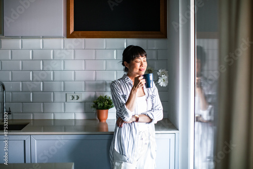 Asian woman enjoying a cup of hot drink in the kitchen