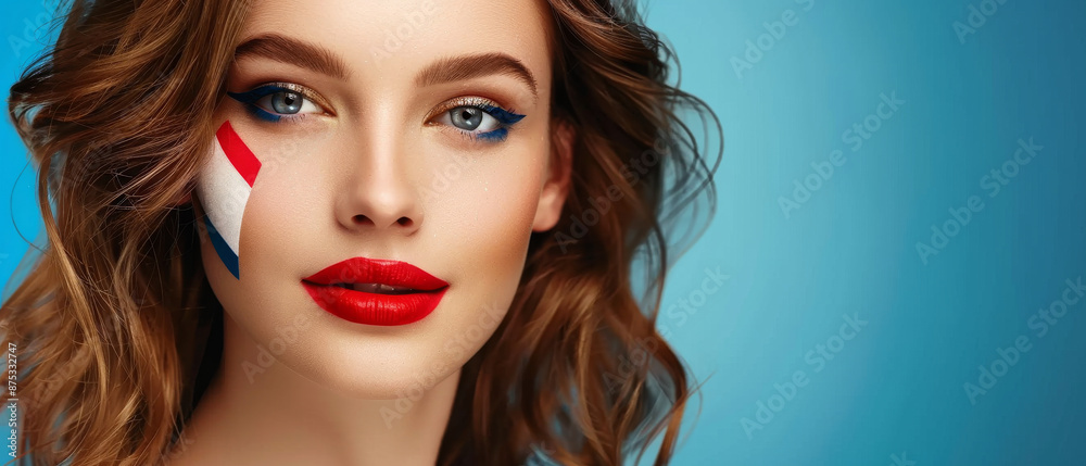 Fototapeta premium A close-up of a woman with vibrant face paint in the colors of the Dutch flag, set against an out-of-focus blue background.