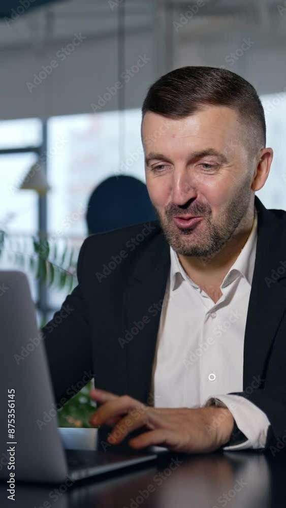 Business meeting via laptop. Businessman talking and smiling while talking before the laptop. Spacious office in blur at the background. Vertical video Business meeting via laptop. Businessman talking and smiling while talking before the laptop. Spacious office in blur at the background. Vertical video